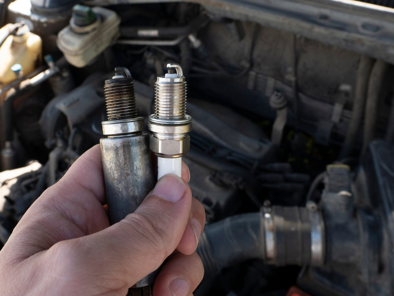 Man Holding old and new car spark plugs on engine background